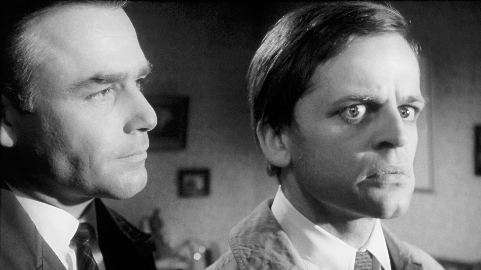 Inspektor Larry Hold (Joachim Fuchsberger, links) steht mit kritischen Blick hinter dem ihm abgewandten Sekretär Edgar (Klaus Kinski), der seinerseits überrascht-erschrocken in die andere Richtung schaut.