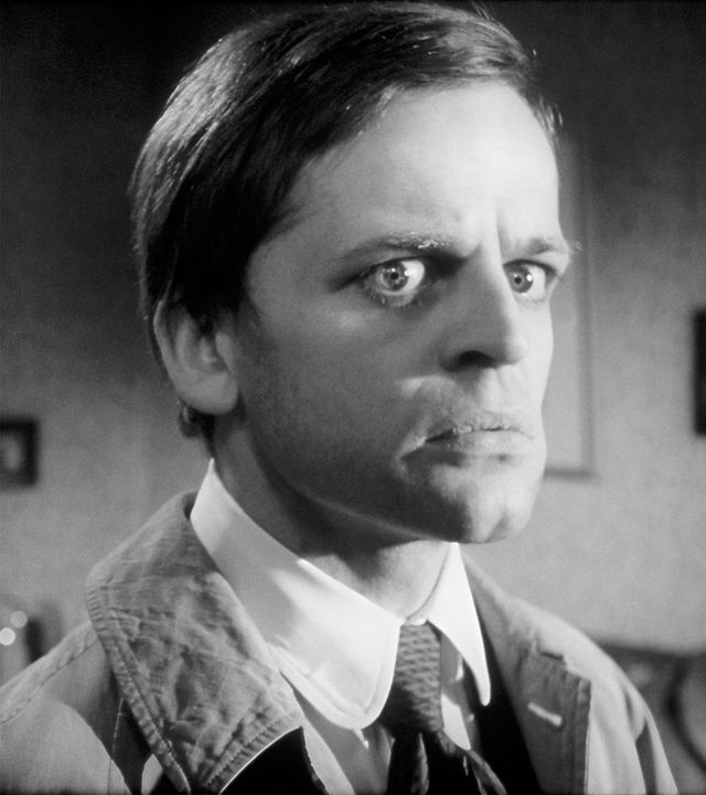 Inspektor Larry Hold (Joachim Fuchsberger, links) steht mit kritischen Blick hinter dem ihm abgewandten Sekretär Edgar (Klaus Kinski), der seinerseits überrascht-erschrocken in die andere Richtung schaut.