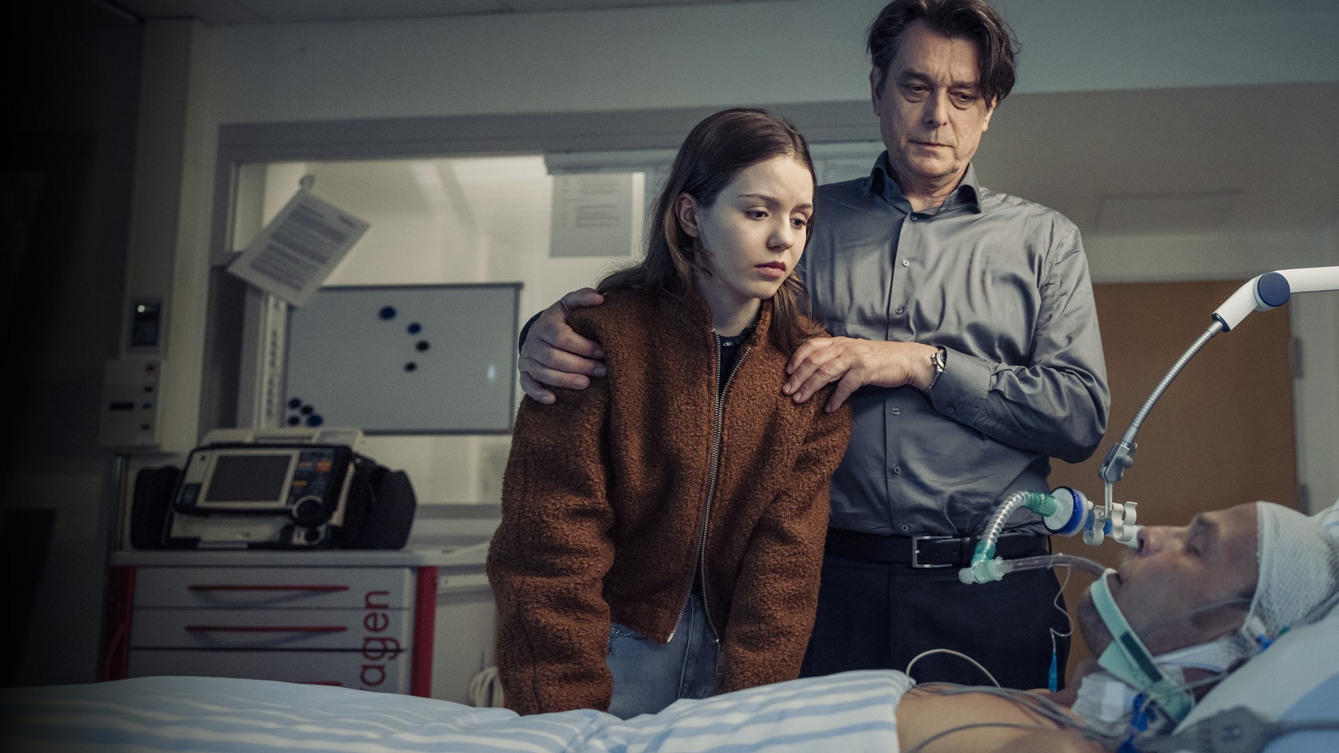 "Die Toten vom Bodensee - Im Schattenreich": Luna Oberländer (Fiona Katharina Neumeier) und Thomas Komlatschek (Hary Prinz) stehen bei Micha Oberländer (Matthias Koeberlin) am Krankenbett.