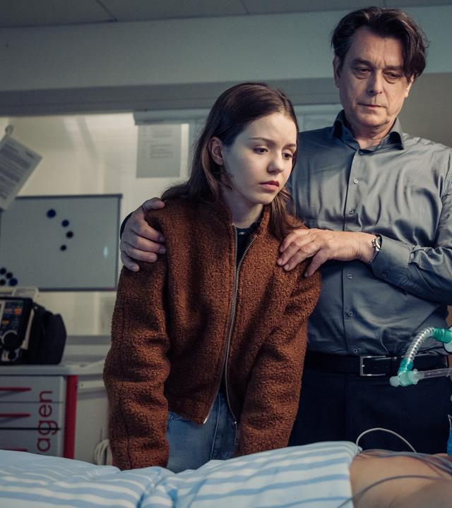 "Die Toten vom Bodensee - Im Schattenreich": Luna Oberländer (Fiona Katharina Neumeier) und Thomas Komlatschek (Hary Prinz) stehen bei Micha Oberländer (Matthias Koeberlin) am Krankenbett.
