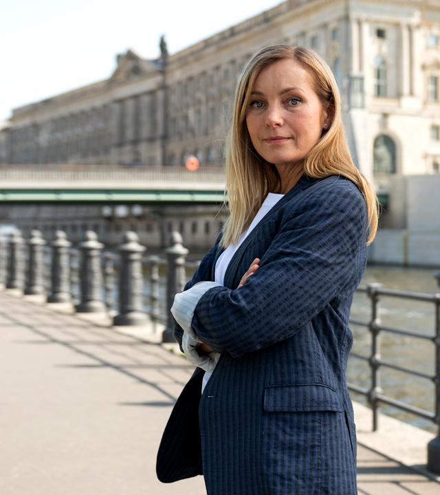 "Die Jägerin - Gegen die Wut": Staatsanwältin Judith Schrader steht mit verschränkten Armen im Freien vor der Spree. Im Hintergrund steht die Berliner Rathausbrücke.