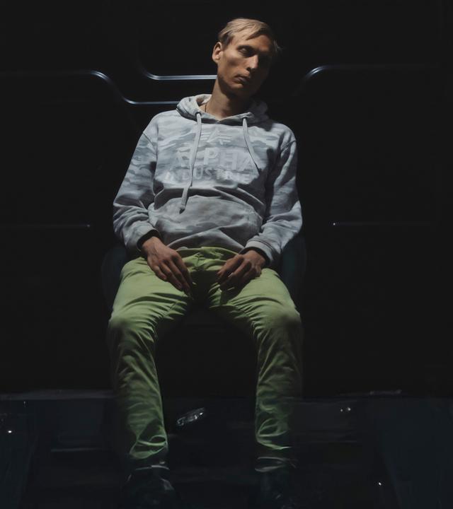 Timo sitzt im Laderaum eines Kleinbusses und schläft.