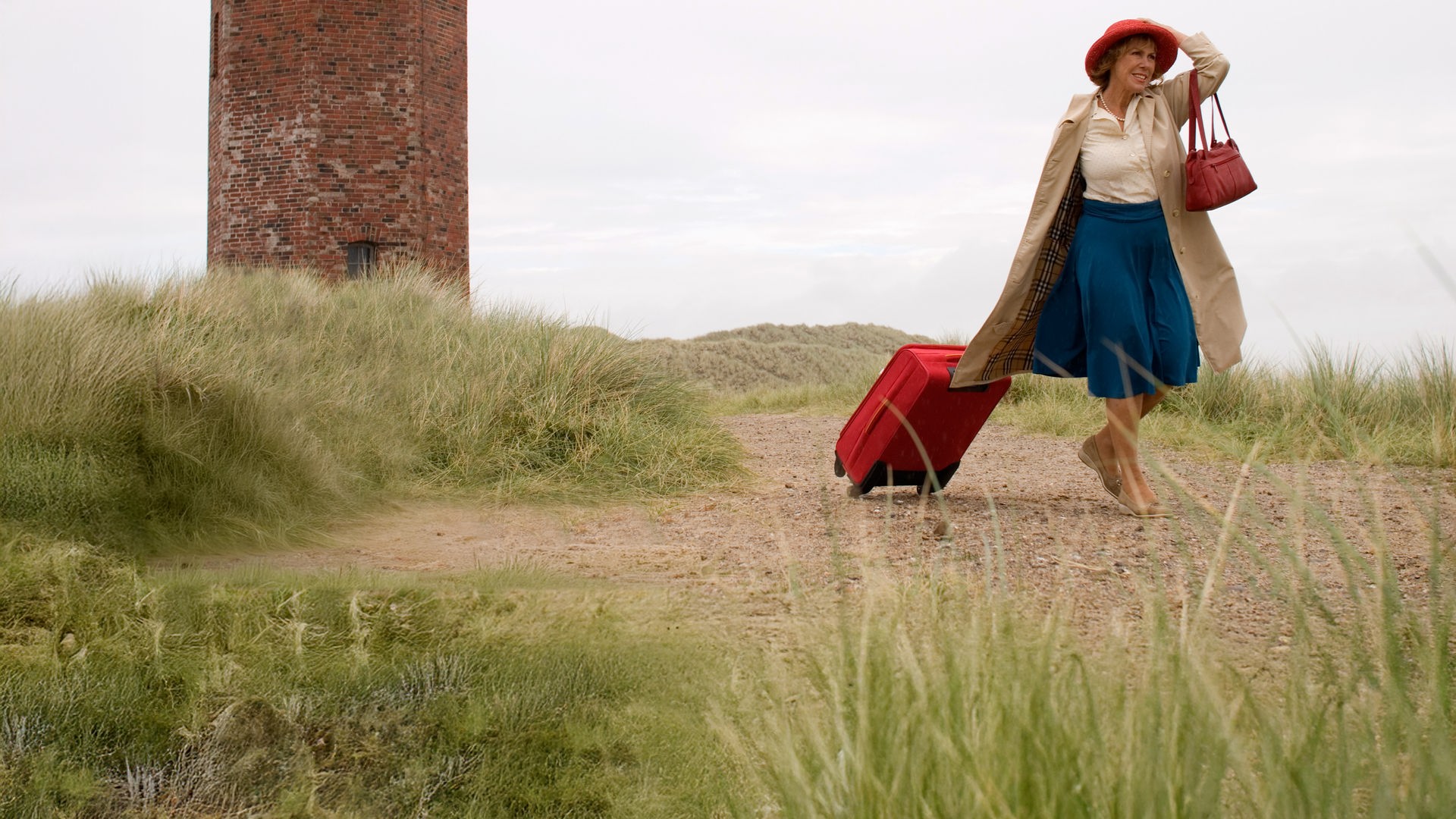 Auf der Insel Sylt läuft Inge (Gaby Dohm) an einem Leuchtturm vorbei. Sie zieht mit der rechten Hand einen Koffer hinter sich her und hält mit der anderen Hand ihren Hut auf dem Kopf fest.