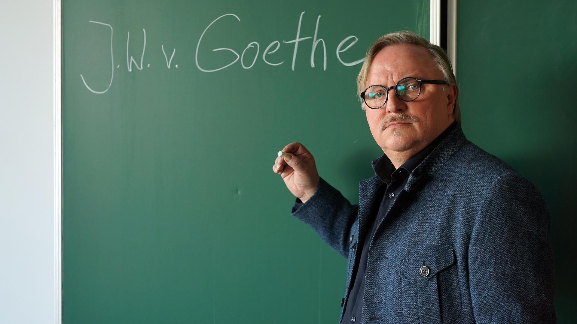 Lehrer Ralph Friesner (Axel Prahl) steht vor der Tafel mit der Aufschrift "J.W.v. Goethe".