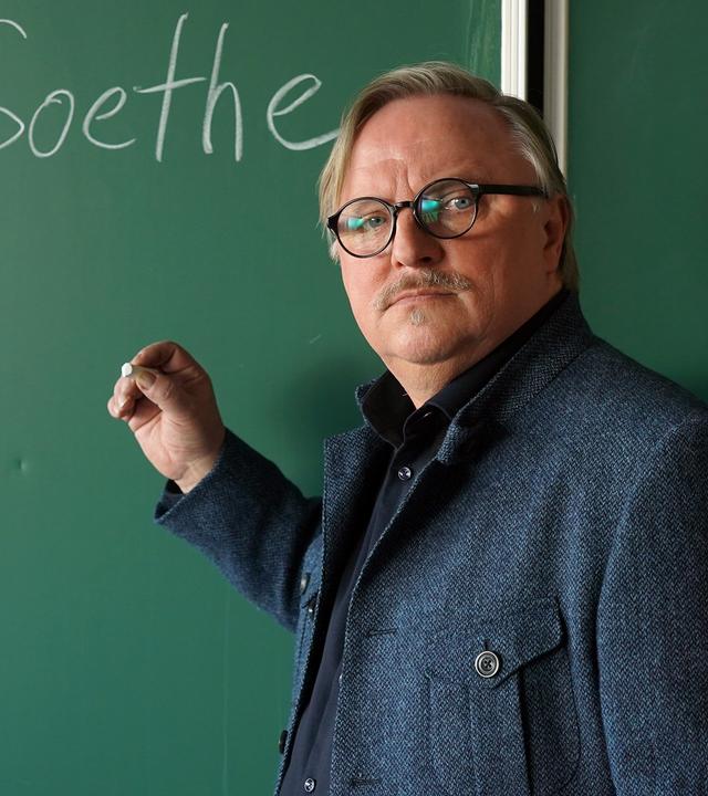 Lehrer Ralph Friesner (Axel Prahl) steht vor der Tafel mit der Aufschrift "J.W.v. Goethe".