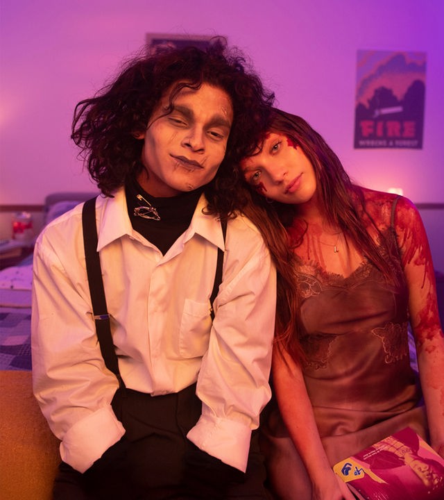  Adam (D'Pharaoh Woon-A-Tai) und Lindy (Maddie Ziegler) sitzen lächelnd nebeneinander auf einem Bett. Er ist als Edward mit den Scherenhänden kostümiert, sie als blutüberströmte Carrie