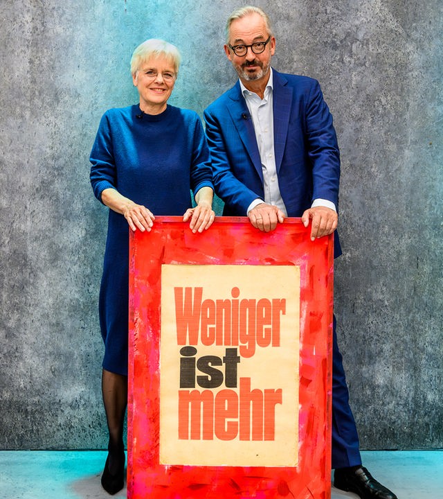 Jan Fleischhauer und Ulrike Herrmann stehen hinter einem Schild auf dem steht: Weniger ist mehr.