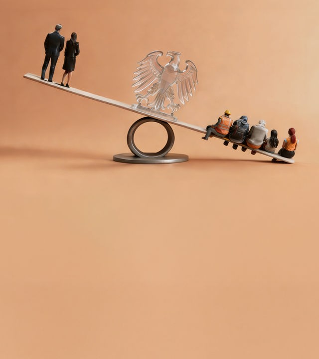 Wippe mit Figuren an beiden Enden. In der Mitte ist ein Bundesadler aus Glas.