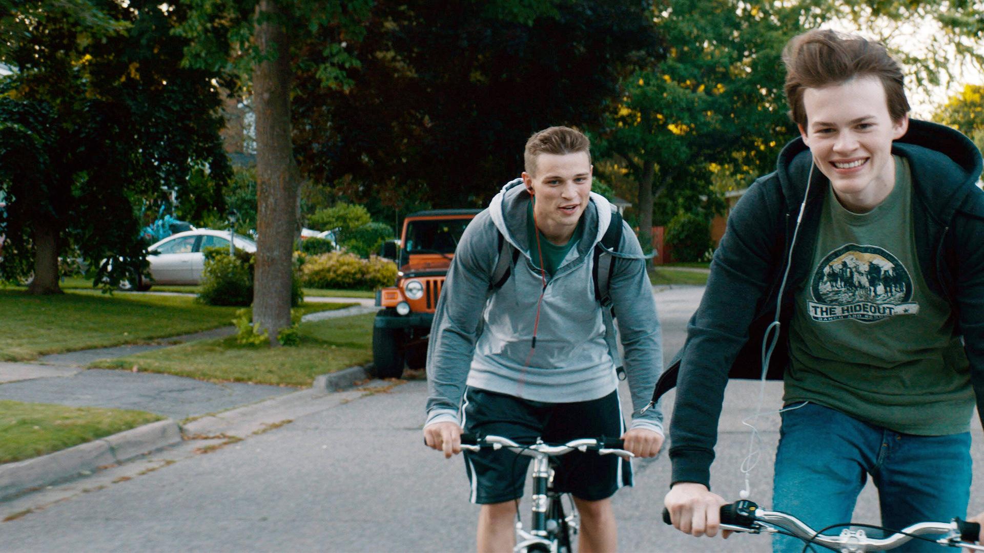 Von links: Ballas (Darren Mann) und Franky (Josh Wiggins) fahren auf dem Fahrrad in Richtung Kamera. Beide lachen.