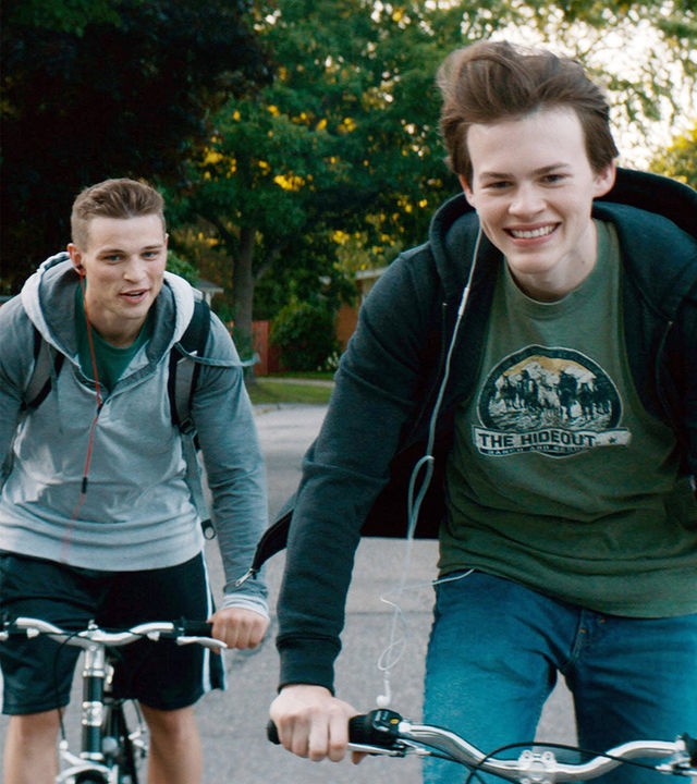 Von links: Ballas (Darren Mann) und Franky (Josh Wiggins) fahren auf dem Fahrrad in Richtung Kamera. Beide lachen.