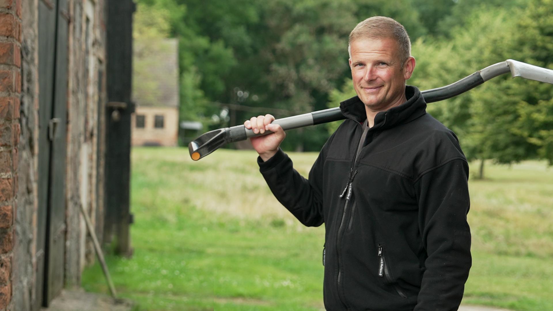 Grenzpolizist Mario Kalski, gekleidet in Arbeitskleidung und mit einer Schaufel über der Schulter, packt an der Grenze im Dorf Schmarsow bei Pasewalk mit an.