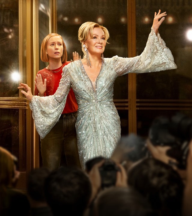Hacks Staffel 3: Deborah Vance (Jean Smart) steht in einem glamourösen, silbernen Paillettenkleid mit ausgebreiteten Armen auf einer Bühne und blickt in ein riesiges, applaudierendes Publikum im Scheinwerferlicht.