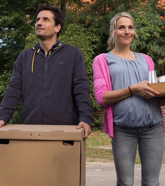 Stefan (Oliver Mommsen, li.) trägt einen Umzugskarton und die schwangere Silke (Tanja Wedhorn, re.) ein Tablett mit Geschirr.