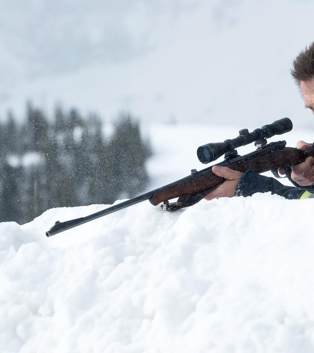 Nels Coxman (Liam Neeson) sitzt hinter einem Schneehaufen und hat seine Sniper in den Händen. Er beobachtet etwas außerhalb des Bildes.