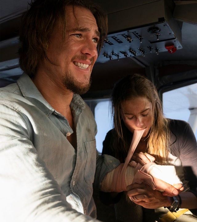 Sara (Allison Williams) und Jackson (Alexander Dreymon) sitzen im Cockpit eines Kleinflugzeuges. Sara legt Jackson einen Druckverband an und hält den Stoff mit ihren Zähnen stramm. Er hat sichtbare Schmerzen und schaut weg.