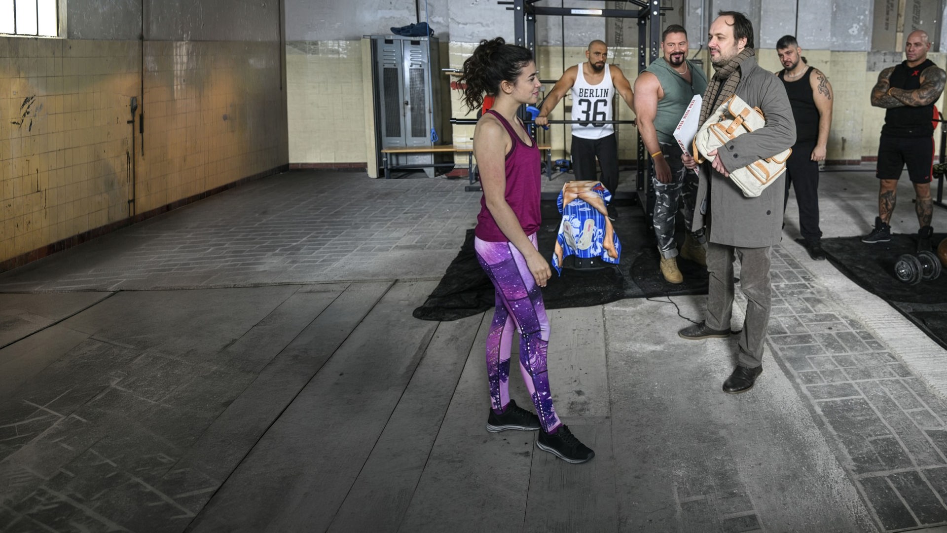 "Hüftkreisen mit Nancy": Nancy (Helen Woigk) und Max (Felix Knopp) stehen sich vor den Geräten des Fitnessstudios gegenüber und werden dabei von den anderen Mitgliedern beobachtet.