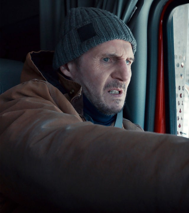 Nahaufnahme: Mike McCann (Liam Neeson) sitzt mit angespanntem Gesichtsausdruck am Steuer eines Lkw. Durch sein Seitenfenster ist verschwommen ein verschneiter Wald zu erkennen.