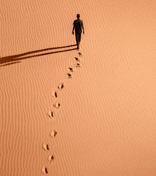 Luftaufnahme: Seydou (Seydou Sarr) schreitet durch die Wüste und hinterlässt Fußspuren im Sand, auf den er einen überdimensionierten Schatten wirft.