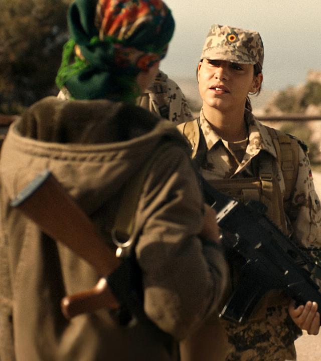 Rojda Xani (Almila Bagriacik, M.) und ihr Kamerad Mark Fuhrmann (Niels Bruno Schmidt, r.) stehen der Peschmergakämpferin Berivan (Zübeyde Bulut, l.) gegenüber. Sie  tragen Tarnuniformen und haben ein Maschinengewehr im Anschlag.