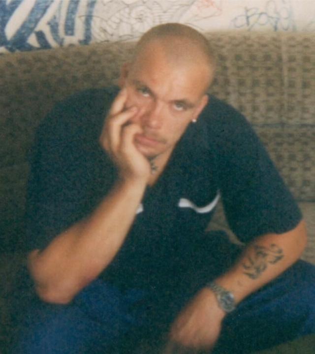 Eichi war als junger Erwachsener rechtsradikal. "Im Osten was Neues": Thomas "Eichi" Eichstätt sitzt als junger Erwachsener in den 90er Jahren auf einer Eckcouch. Graffitigekritzel befindet sich auf der Wand hinter ihm.