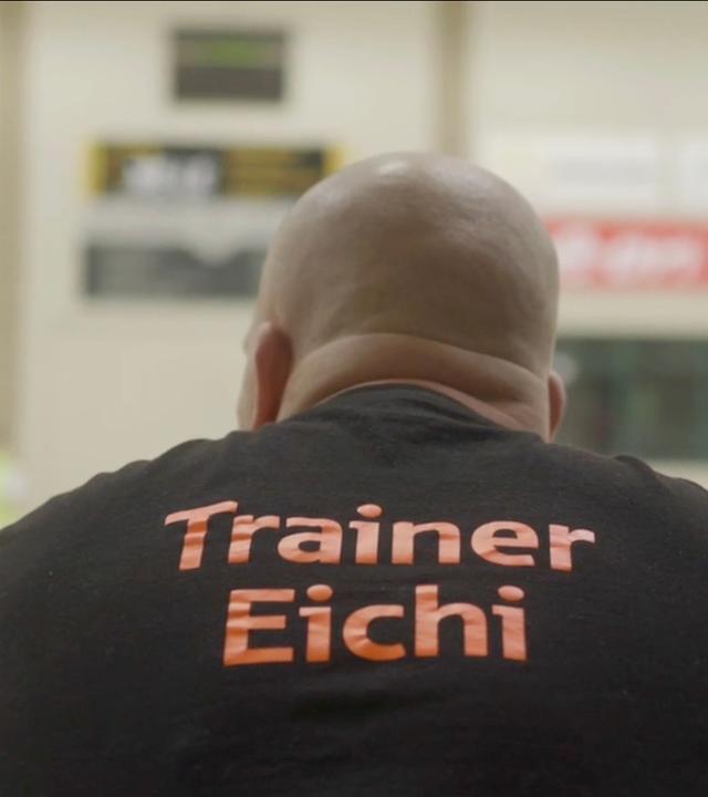 Eichi war als junger Erwachsener rechtsradikal. "Im Osten was Neues": Thomas "Eichi" Eichstätt sitzt als junger Erwachsener in den 90er Jahren auf einer Eckcouch. Graffitigekritzel befindet sich auf der Wand hinter ihm.