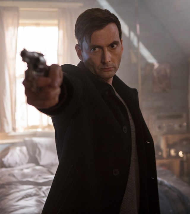 Cale Erendreich (David Tennant) steht mit gezogener Waffe in einem Schlafzimmer.