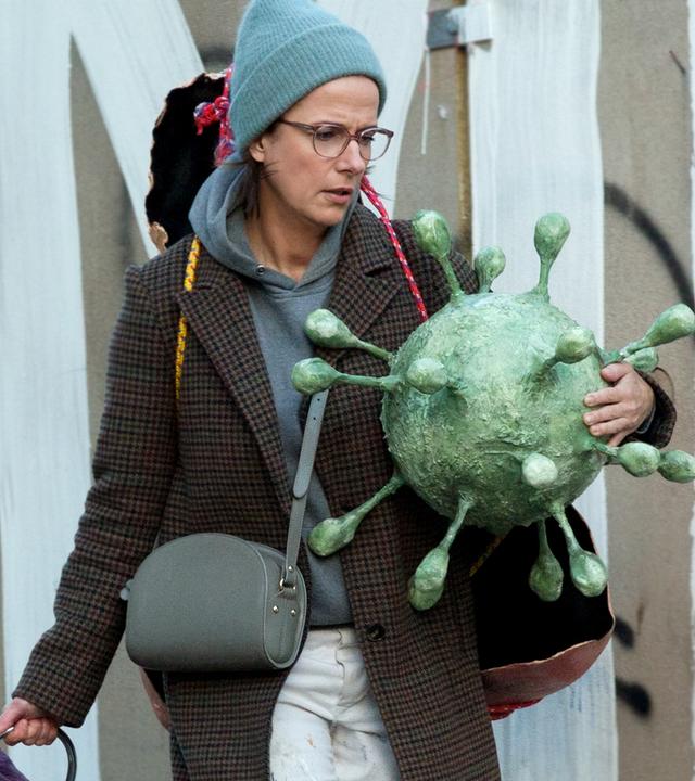 Die Schaufensterdekorateurin Tanja (Claudia Michelsen) läuft mit Requisiten bepackt auf einer Straße, die an einem Bauzaun entlang führt.