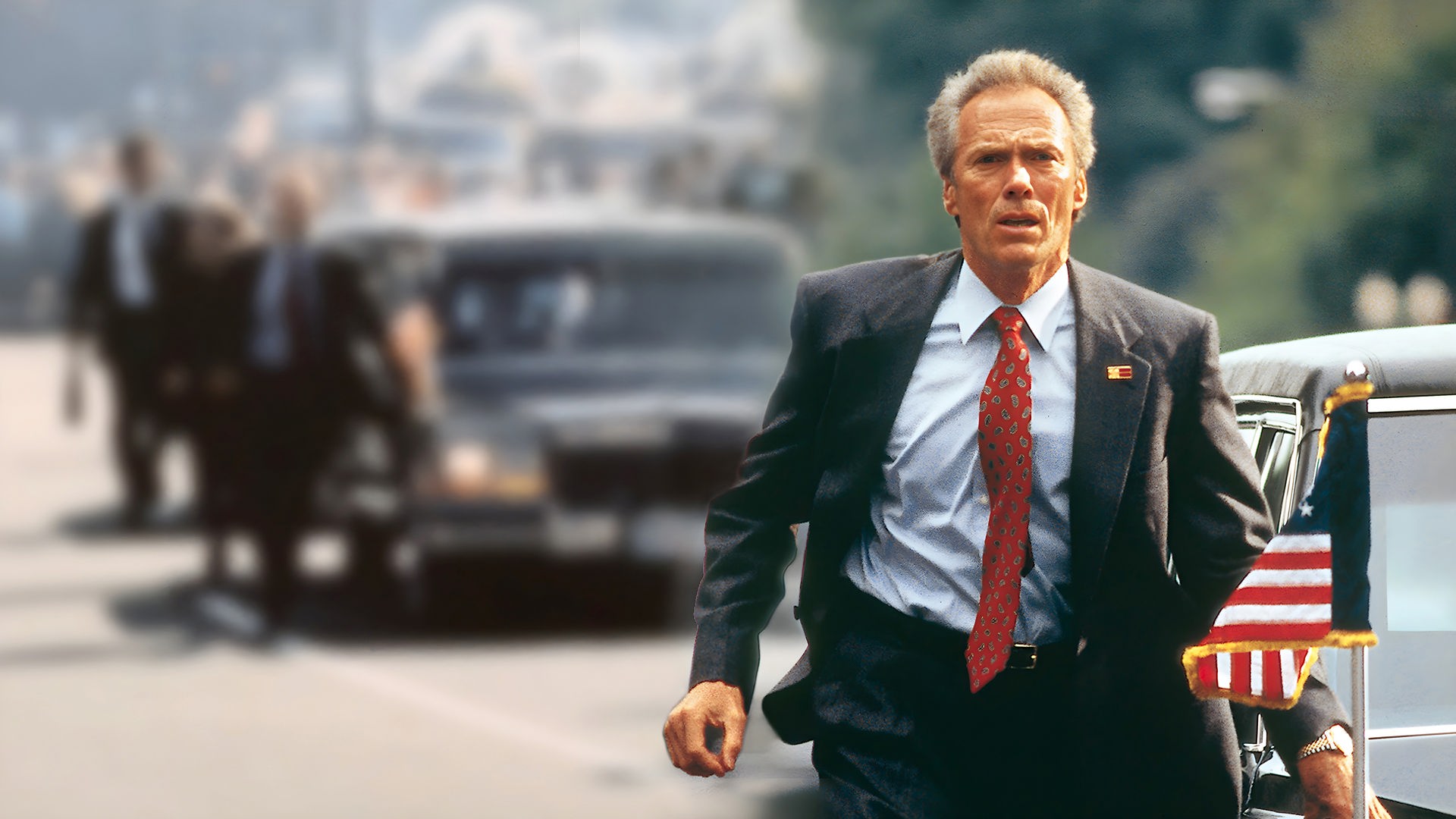 "In The Line Of Fire - Die zweite Chance": Agent Horrigan (Clint Eastwood) läuft neben einer schwarzen Limousine mit US-amerikanischen Flaggen und schaut konzentriert in die Ferne.