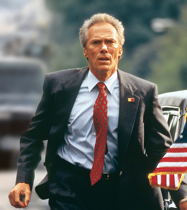 "In The Line Of Fire - Die zweite Chance": Agent Horrigan (Clint Eastwood) läuft neben einer schwarzen Limousine mit US-amerikanischen Flaggen und schaut konzentriert in die Ferne.