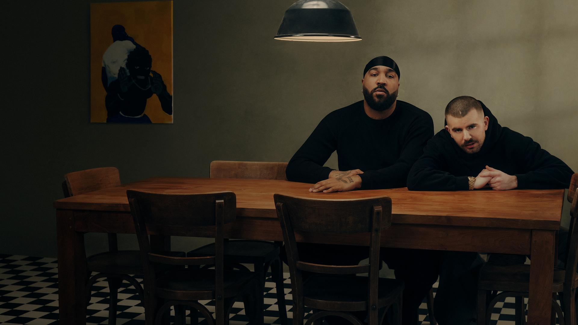 OG Keemo und Funkvater Frank sitzen an einem Küchentisch unter einer Lampe und blicken in die Kamera