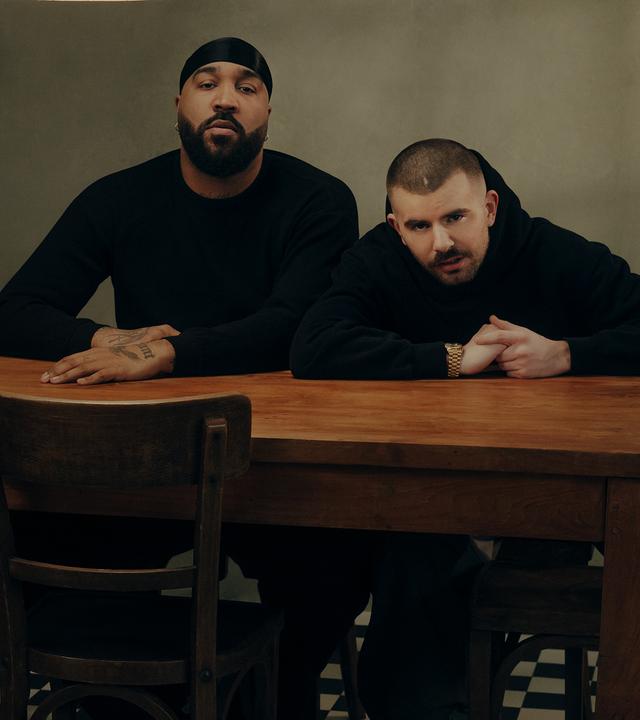 OG Keemo und Funkvater Frank sitzen an einem Küchentisch unter einer Lampe und blicken in die Kamera
