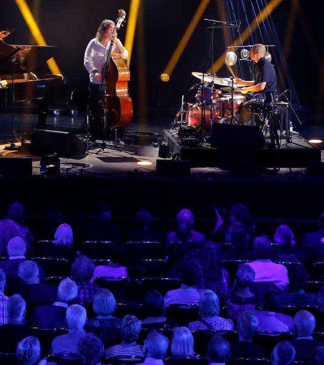 Jazztrio auf einer stimmungsvoll ausgeleuchteten Bühne, links der Pianist Michael Wollny am Flügel, in der Mitte Kontrabassist Tim Lefebvre und rechts Eric Schaefer am Schlagzeug.
