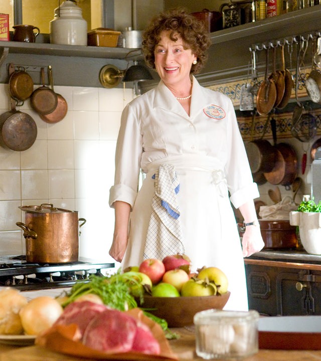 Während ihrer Zeit in Paris begeistert sich Julia Child (Meryl Streep) immer mehr für die französische Küche. Sie beschließt, bei einem Kochbuch mitzuwirken, das noch Jahre später Leute begeistern wird. "Julie & Julia": Julia Child (Meryl Streep) steht mit einer Schürze in einer Küche und schaut lächelnd in die Ferne. Auf dem Tresen vor ihr sind dabei verschiedene Lebensmittel ausgebreitet.