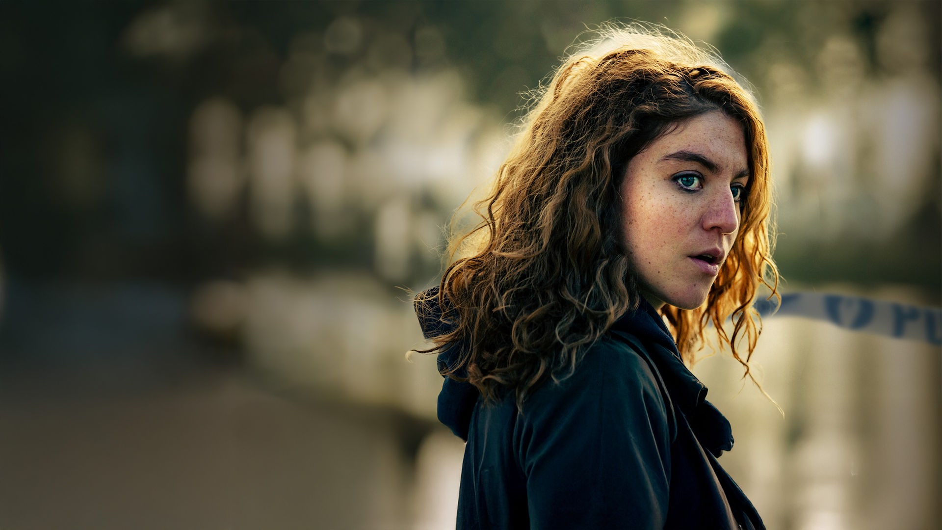 Juliet: Die Hauptkommissarin Juliet Dumon (Charlotte De Bruyne) steht mit nachdenklichem, leicht besorgtem Blick an einem nebligen Tatort. Im verschwommenen Hintergrund ist ein blau-weißes Absperrband mit der Aufschrift „POLITIE“ gespannt.