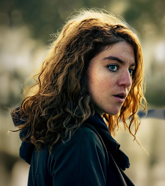 Juliet: Die Hauptkommissarin Juliet Dumon (Charlotte De Bruyne) steht mit nachdenklichem, leicht besorgtem Blick an einem nebligen Tatort. Im verschwommenen Hintergrund ist ein blau-weißes Absperrband mit der Aufschrift „POLITIE“ gespannt.