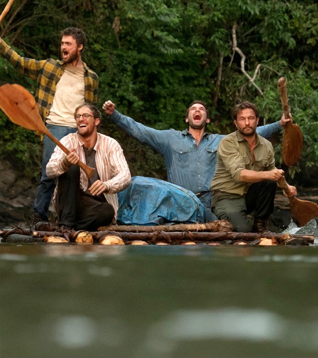 Yossi (Daniel Radcliffe), Marcus (Joel Jackson), Kevin (Alex Russell), alle mit ausgestreckten Armen jubelnd, und Karl (Thomas Kretschmann) sitzen auf einem, im Fluss treibenden, Floß.