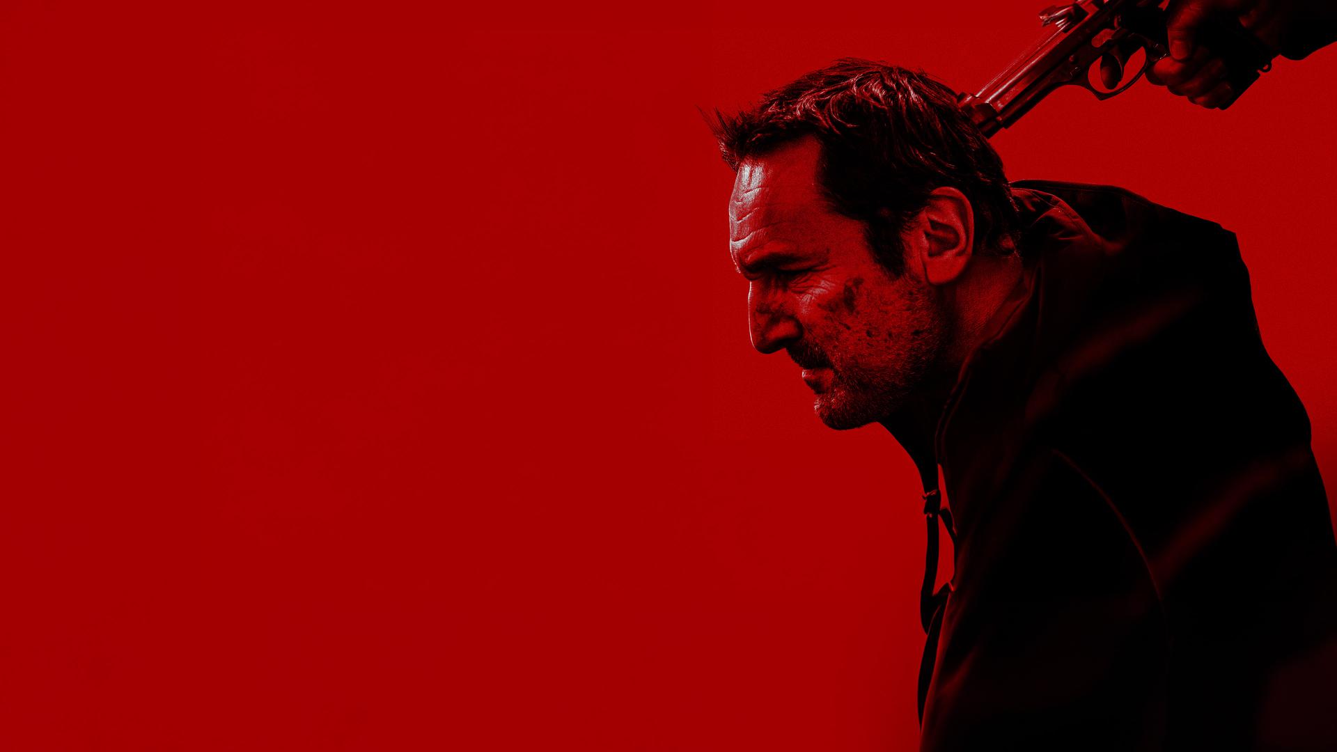 Schwarz-Rotes Foto: Blick von der Seite auf Mathieu Roussel (Gilles Lellouche), dem jemand hält eine Pistole an seinen Hinterkopf hält.
