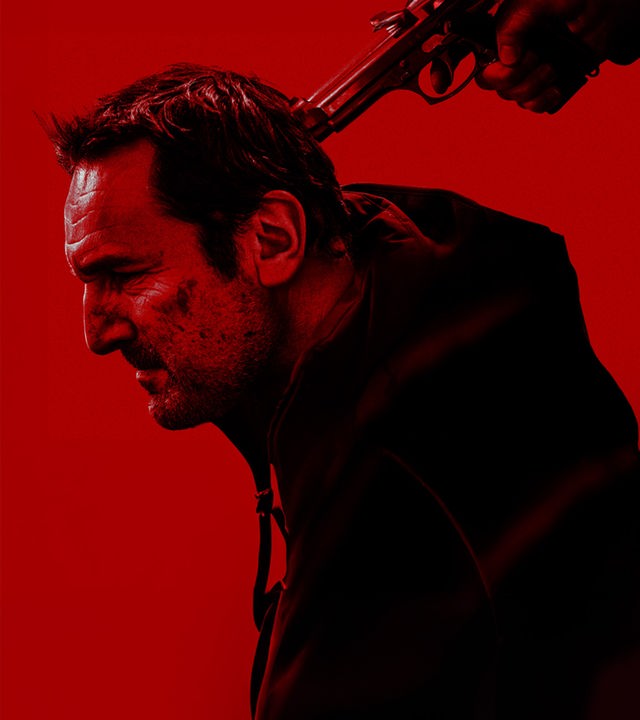 Schwarz-Rotes Foto: Blick von der Seite auf Mathieu Roussel (Gilles Lellouche), dem jemand hält eine Pistole an seinen Hinterkopf hält.