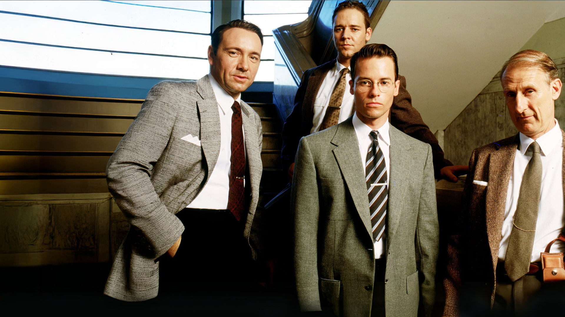 Jack Vincennes (Kevin Spacey), Bud White (Russell Crowe), Ed Exley (Guy Pearce) und Dudley Smith (James Cromwell) stehen auf einer Treppe und blicken nach vorne.