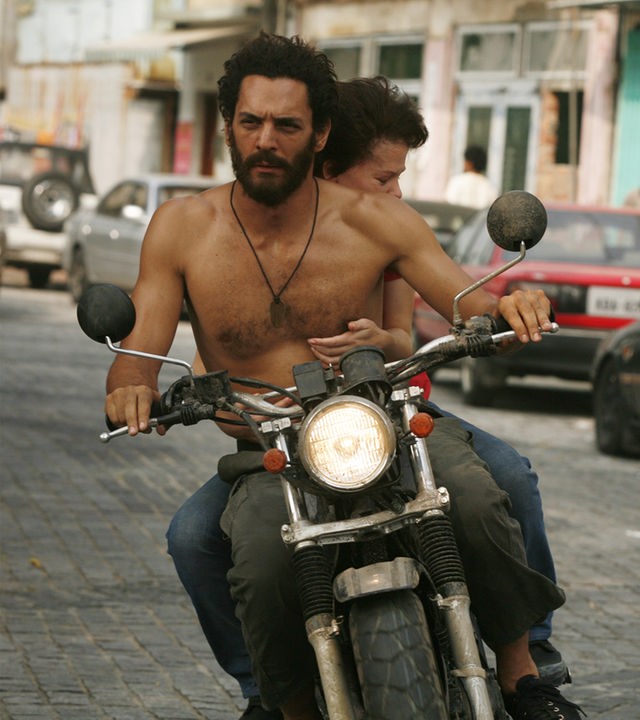 "Largo Winch - Tödliches Erbe": Largo (Tomer Sisley) fährt, Oberkörper frei, mit dem Motorrad durch die Stadt. Hinter ihm sitzt Lea (Mélanie Thierry) und hält sich an ihm fest.