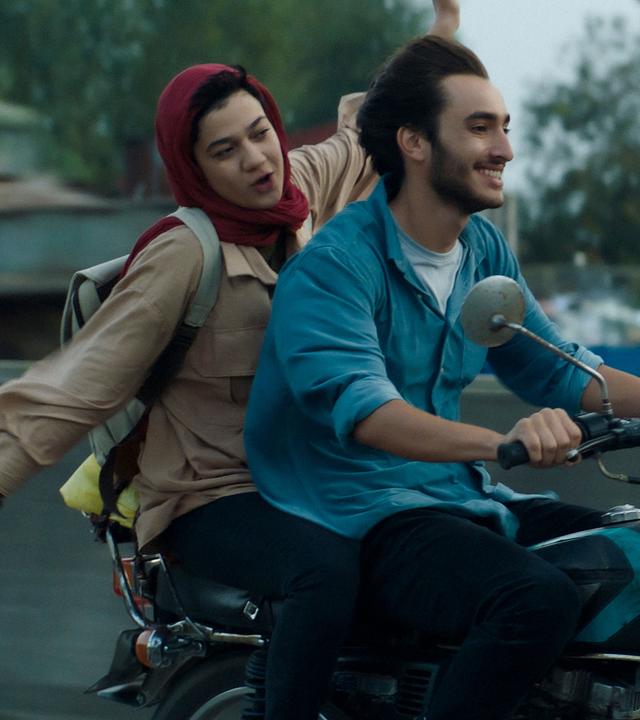 Narges (Sadaf Asgari) sitzt hinter Amir (Hamid Reza Abbasi) auf einem Motorrad und breitet die Arme au