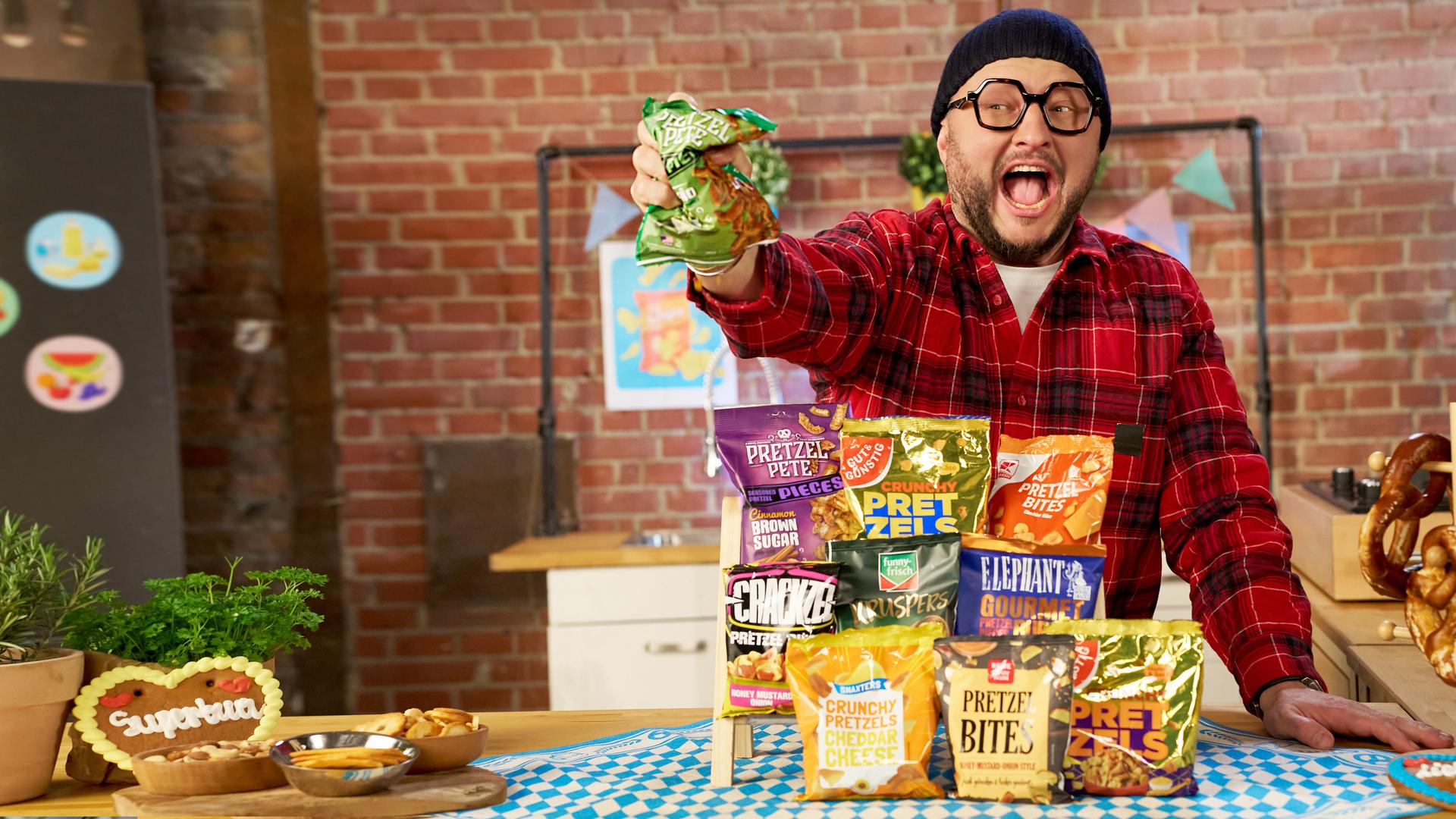 Sebastian Lege steht an einem Tisch, vor ihm liegen diverse Packungen Pretzel Bites. 