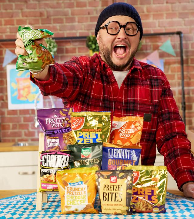 Sebastian Lege steht an einem Tisch, vor ihm liegen diverse Packungen Pretzel Bites. 