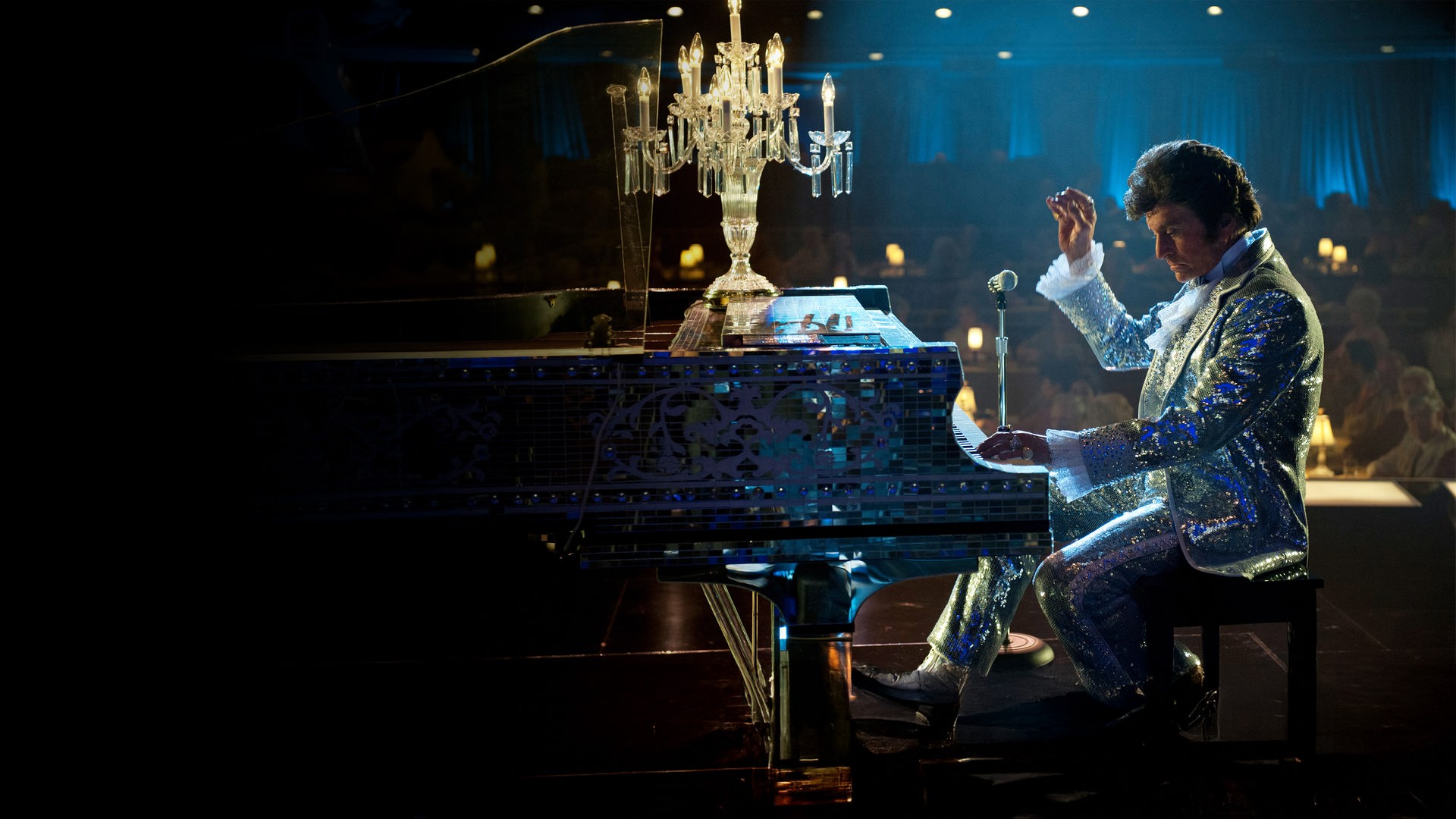 Liberace (Michael Douglas) sitzt in einem glitzerndem Anzug auf einer Bühne und spielt Klavier. Auf dem Musikinstrument steht ein elektrischer Kerzenleuchter. 