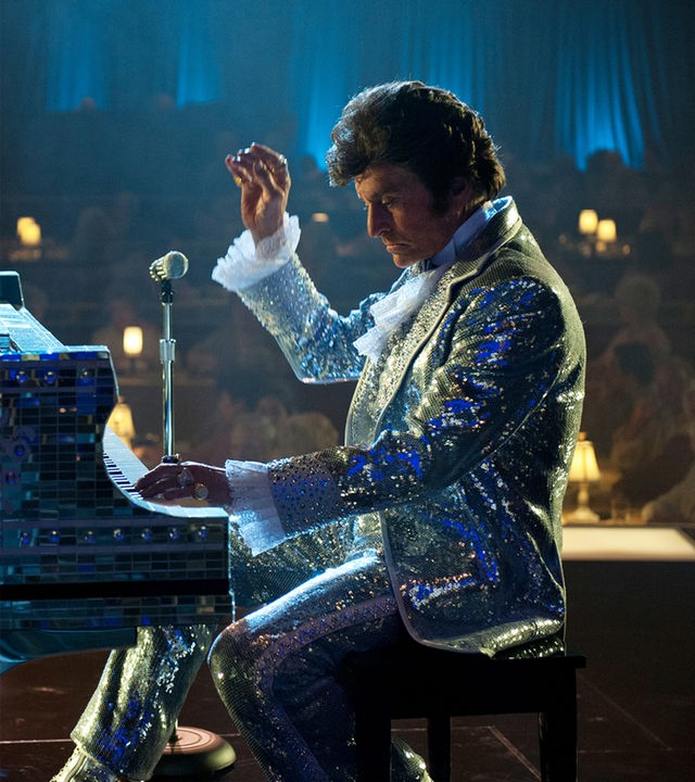 Liberace (Michael Douglas) sitzt in einem glitzerndem Anzug auf einer Bühne und spielt Klavier. Auf dem Musikinstrument steht ein elektrischer Kerzenleuchter. 