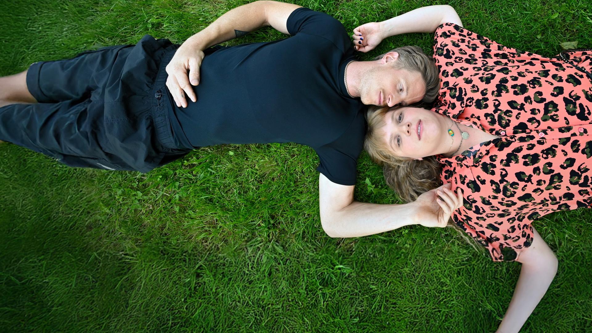 Timo Neuwirth (Golo Euler) und Jenny Fromm (Stefanie Reinsperger) liegen auf einer Wiese mit dem Kopf zueinander. 