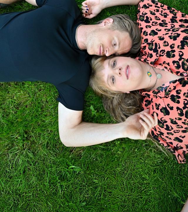 Timo Neuwirth (Golo Euler) und Jenny Fromm (Stefanie Reinsperger) liegen auf einer Wiese mit dem Kopf zueinander. 