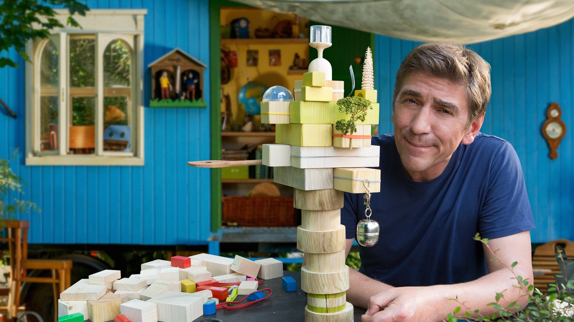 Fritz sitzt vor einem Architekturmodell aus Bauklötzen - im Hintergrund der Bauwagen