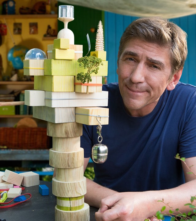 Fritz sitzt vor einem Architekturmodell aus Bauklötzen - im Hintergrund der Bauwagen