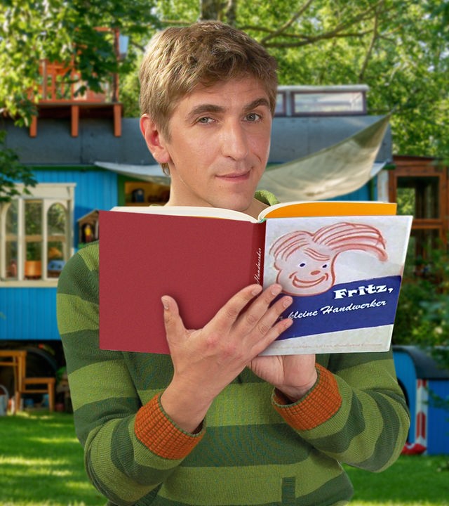 Fritz steht vor dem Bauwagen und hält ein Buch in den Händen